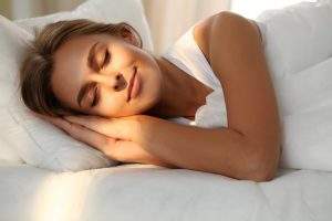 Beautiful young woman sleeping while lying in bed comfortably and blissfully. Sunbeam dawn on her face